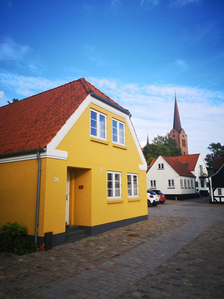 Maison jaune au Danemark avec un clocher en arrière plan
