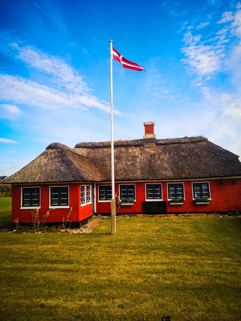 Maison rouge au toit de chaume avec un drapeau danois flottant sous un beau ciel bleu au Danemark
