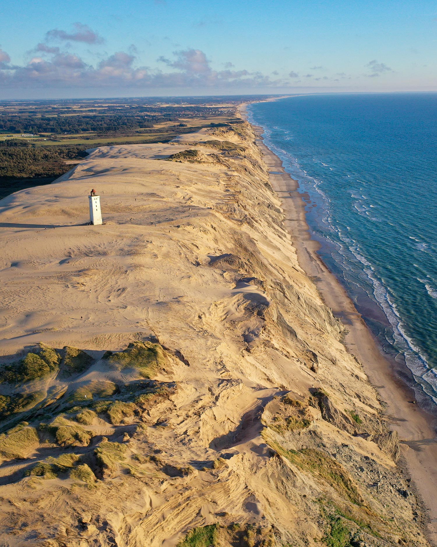 Grande plage et dunes sablés au Danemark avec un petit phare au milieu